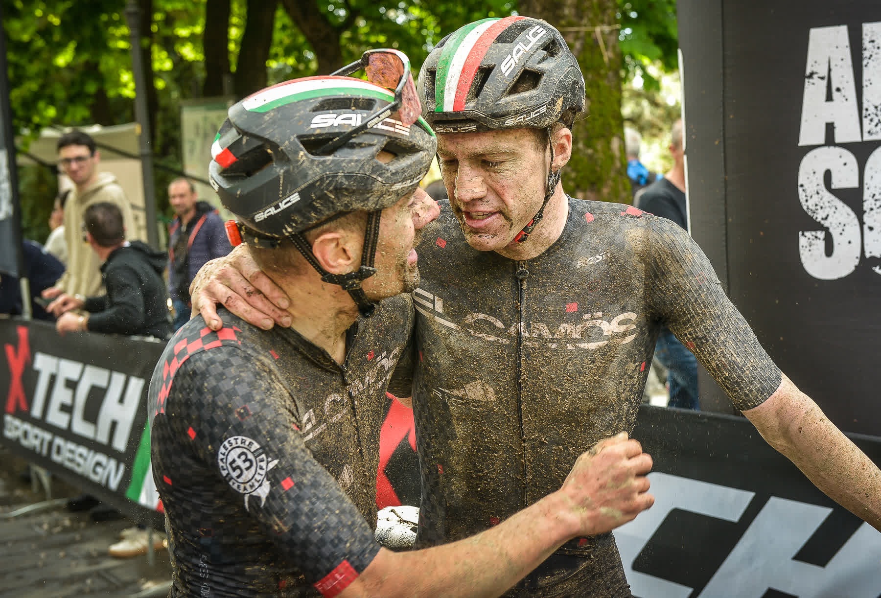 Due ciclisti coperti di fango si abbracciano all'arrivo della Gran Fondo MTB XTech Città di Brescia.